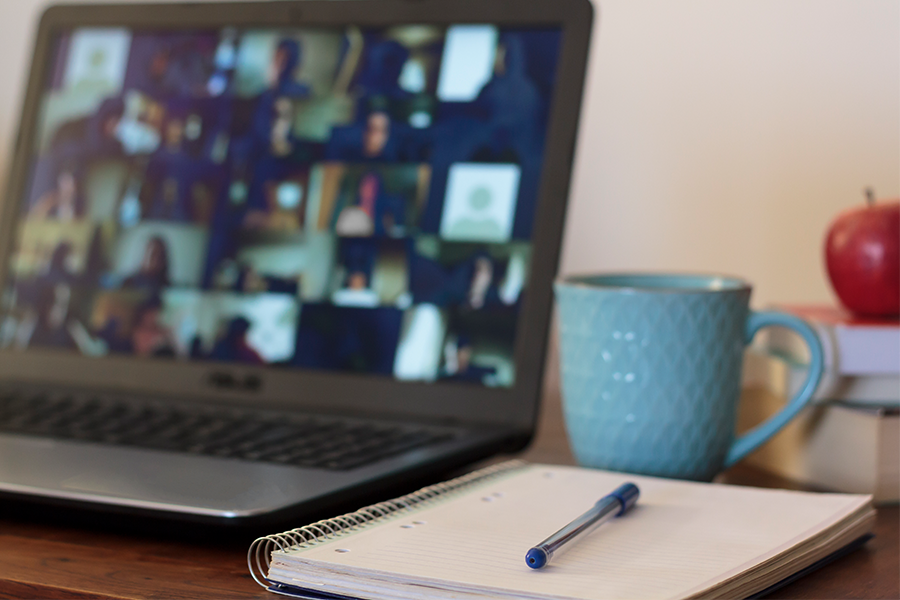 Note pad by laptop with virtual meeting on screen