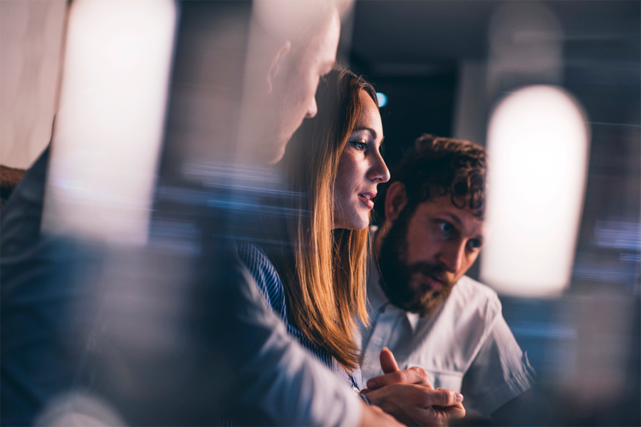 Two businessmen and businesswoman working late in a cafe. They are using laptop computer and talking.
