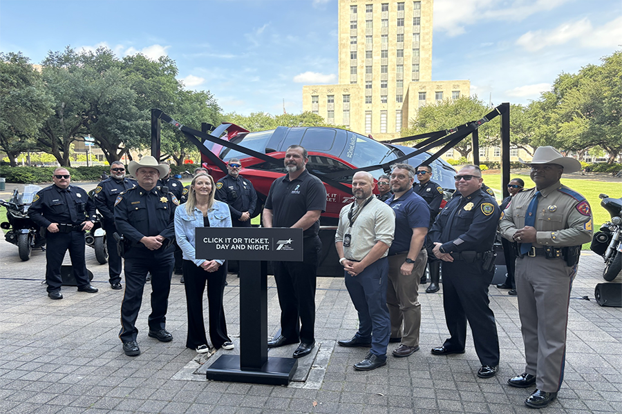 Group of people standing behind a podium with a car behind them