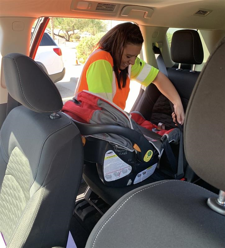 Smiling woman installing car seat A woman in a safety vest installs a car seat into a vehicle.