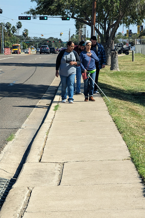 Visually impaired woman with cane and guide A visually impaired woman walks down a sidewalk with a cane and guide.