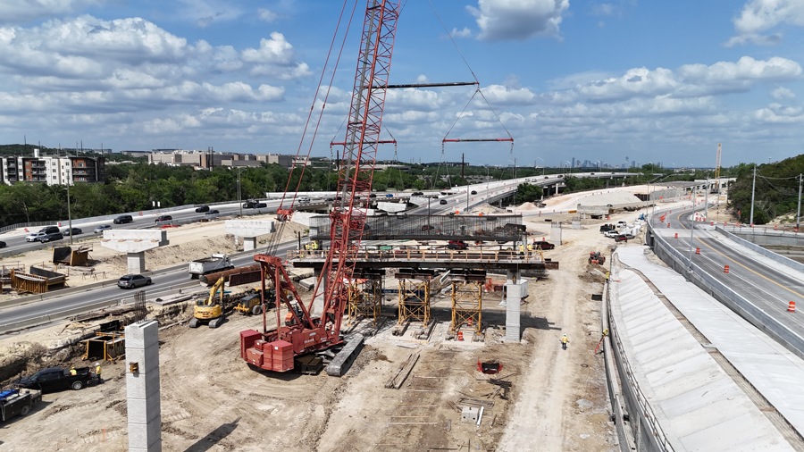 A crane carefully places a rebar cap cage onto recently completed columns for a portion of a ramp bridge near the "Y" interchange. In the final configuration, drivers will be able to use this bridge to reach US 290 from SH 71 after passing through a Single Point Urban Interchange.  May 2025